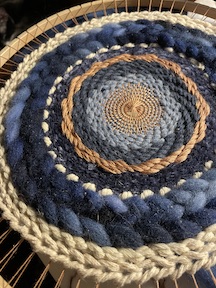 blue, cream, and tan yarns in a circular mandala weaving inside a wooden hoop loom